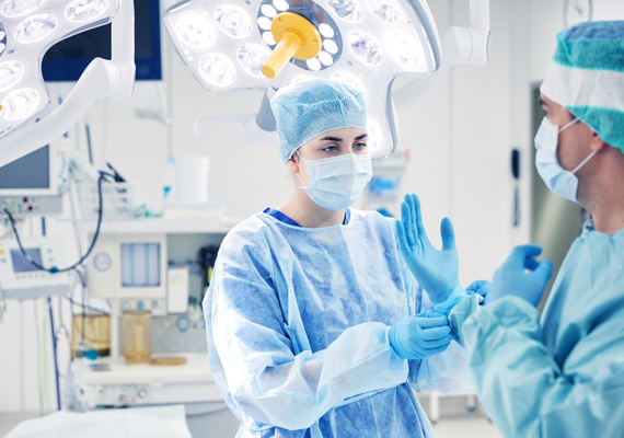 Imagen de un auxiliar ayudando a ponerse los guantes al médico